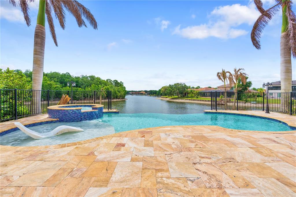 An infinity pool and hot tub overlook a canal with palm trees and houses nearby — 10603 CAYMAN ISLE COURT, TAMPA, FL