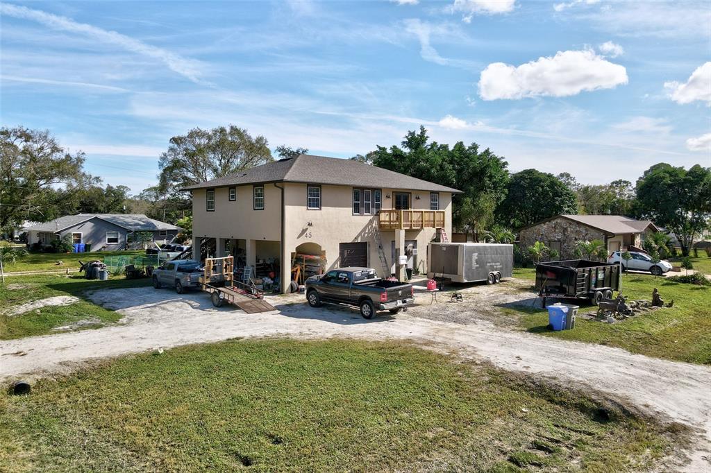 An elevated two-story house with a wooden deck, multiple vehicles, and trailers parked outside — 45 S PINE STREET, FELLSMERE, FL