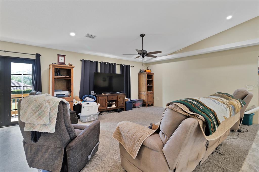 A living room with carpeted floors, a vaulted ceiling, a ceiling fan, and a television console — 45 S PINE STREET, FELLSMERE, FL