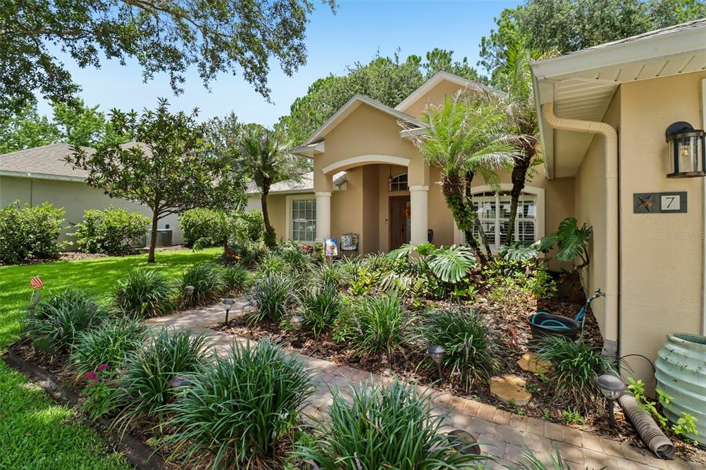 A tan house with a brick walkway, tropical landscaping, and a covered front entryway — 7 PRAIRIEVIEW LANE, ORMOND BEACH, FL