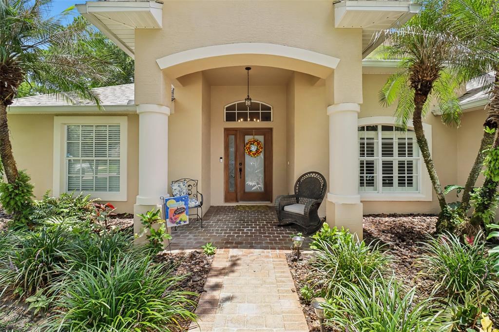 A brick walkway leads to the covered front entrance of a tan house with columns — 7 PRAIRIEVIEW LANE, ORMOND BEACH, FL