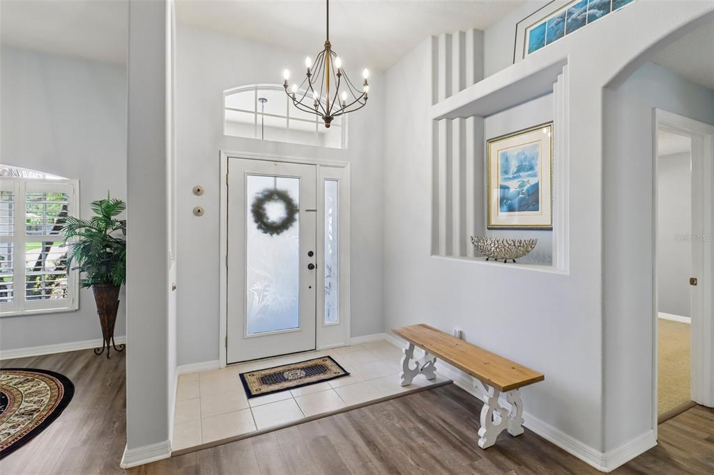 A bright entryway features a white front door, a wooden bench, and a chandelier — 7 PRAIRIEVIEW LANE, ORMOND BEACH, FL