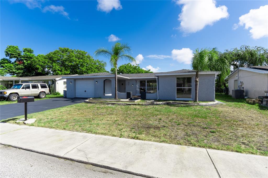 A single-story gray house with a garage, palm trees, and a driveway under a blue sky — 7015 POTOMAC DRIVE, PORT RICHEY, FL