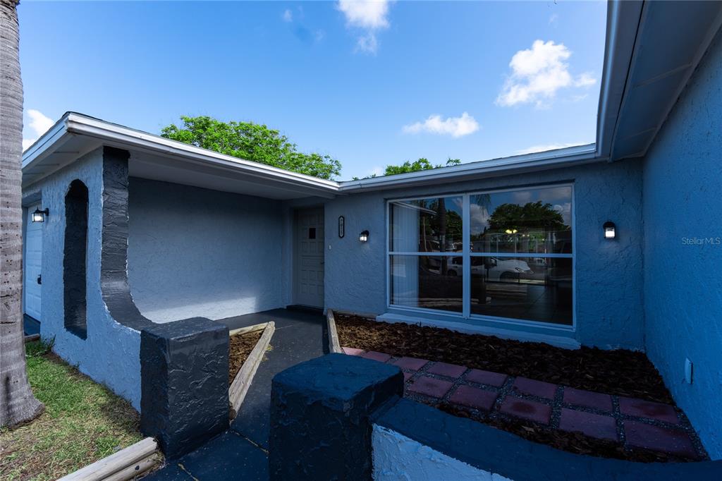 The exterior of a blue house features a covered entryway, a large window, and landscaping — 7015 POTOMAC DRIVE, PORT RICHEY, FL