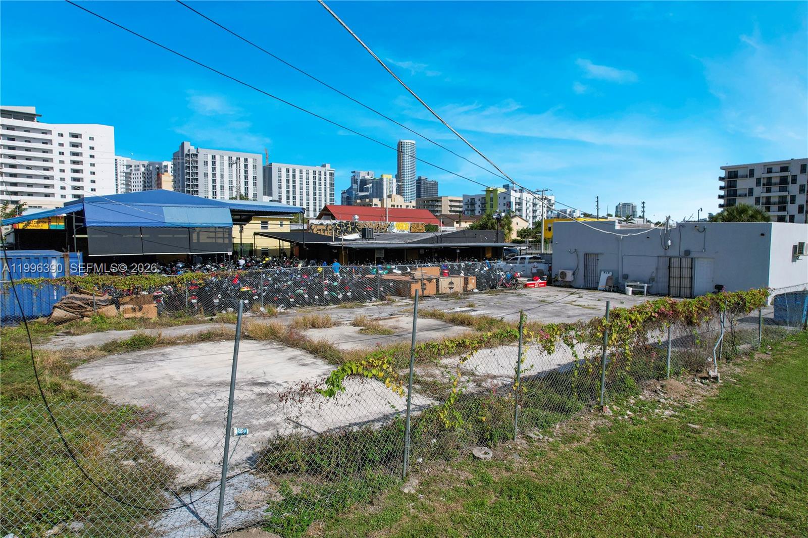 A fenced, paved vacant lot sits in front of a building with a blue canopy — 727 W Flagler St, Miami FL 33130, MIAMI, FL
