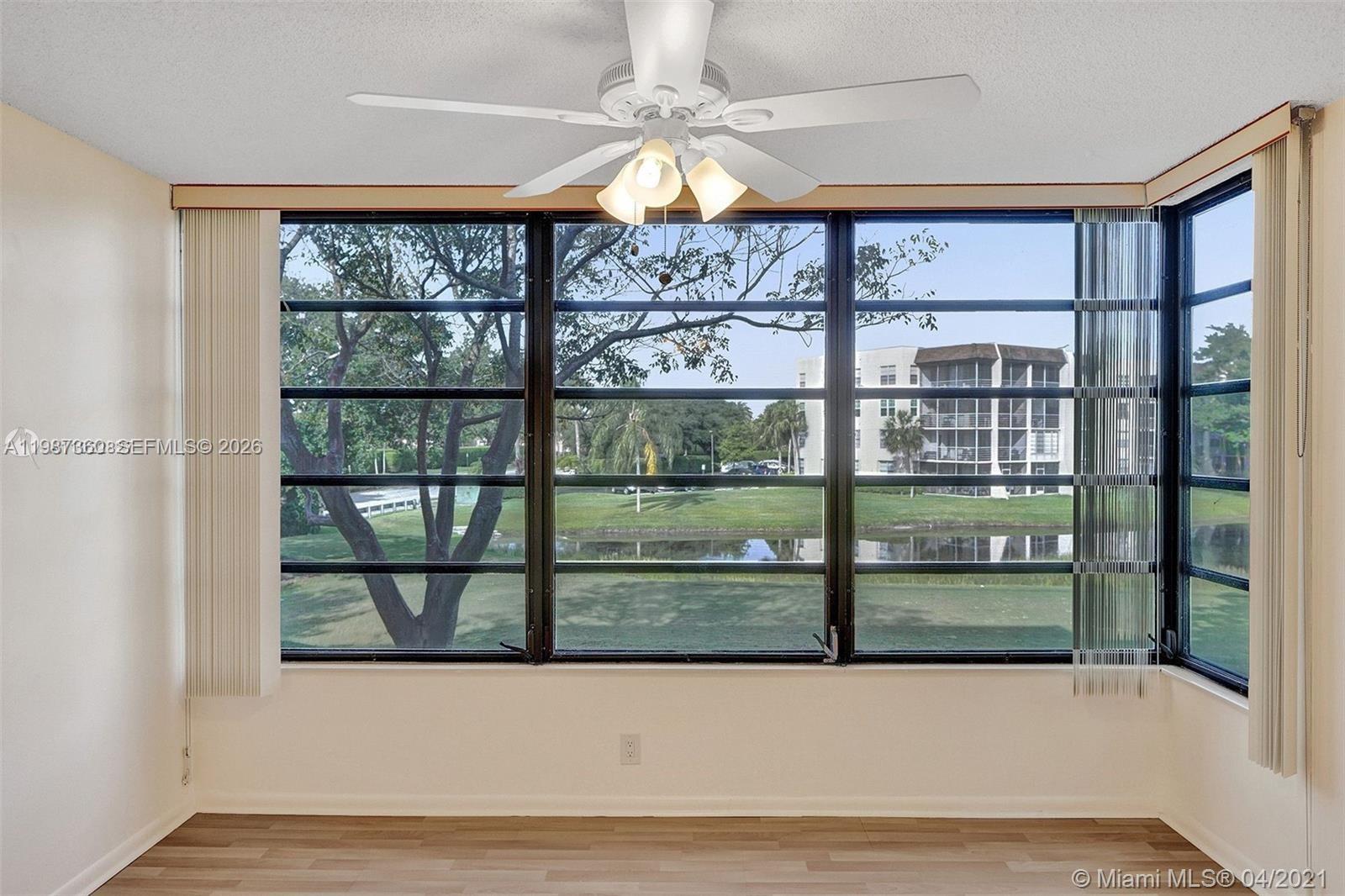 An empty room features a ceiling fan, light-colored flooring, and large windows overlooking a lake — 1715 Whitehall Dr # 202, Davie FL 33324, DAVIE, FL