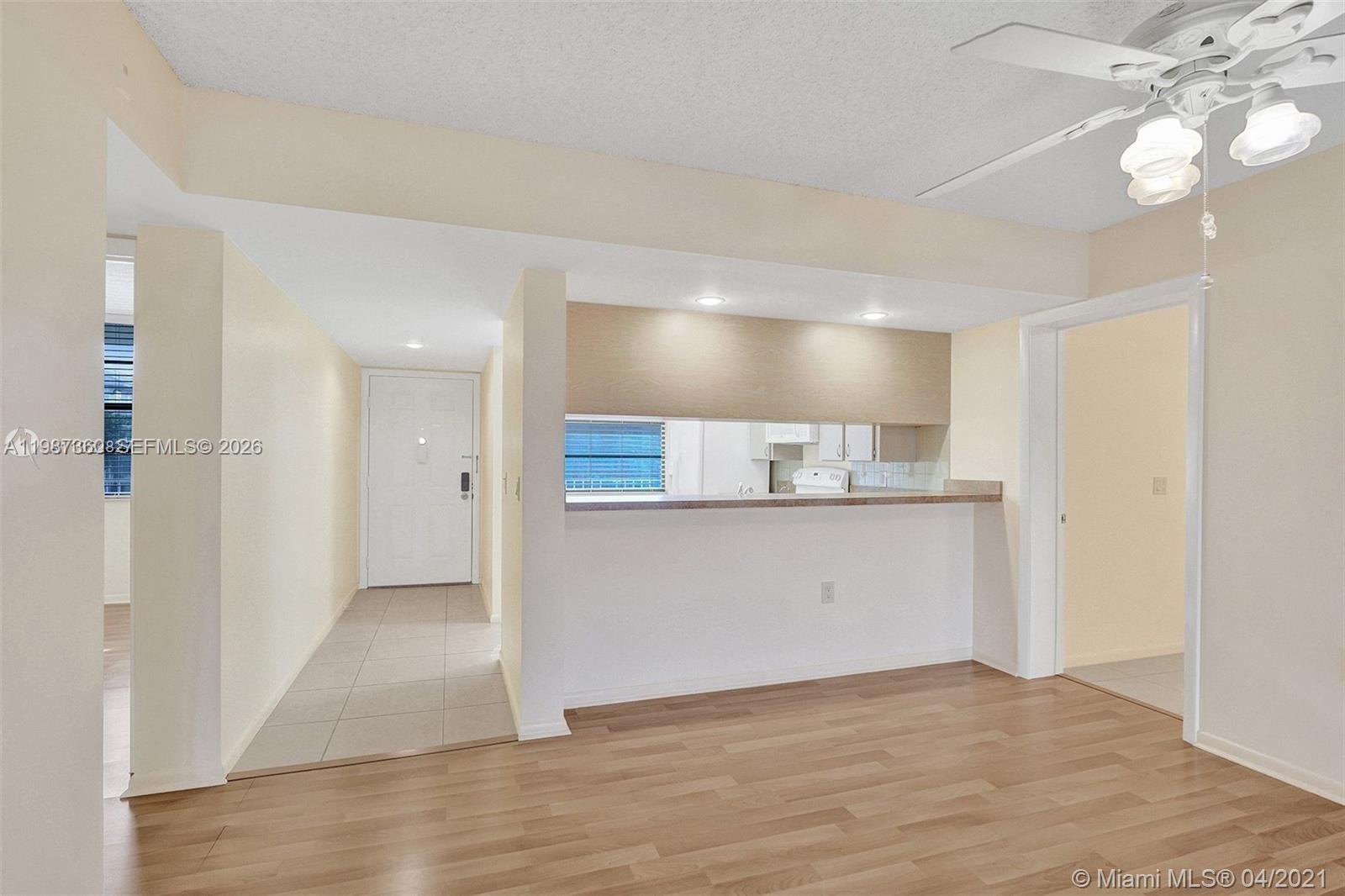 A dining area with wood flooring features a kitchen pass-through window and a ceiling fan — 1715 Whitehall Dr # 202, Davie FL 33324, DAVIE, FL