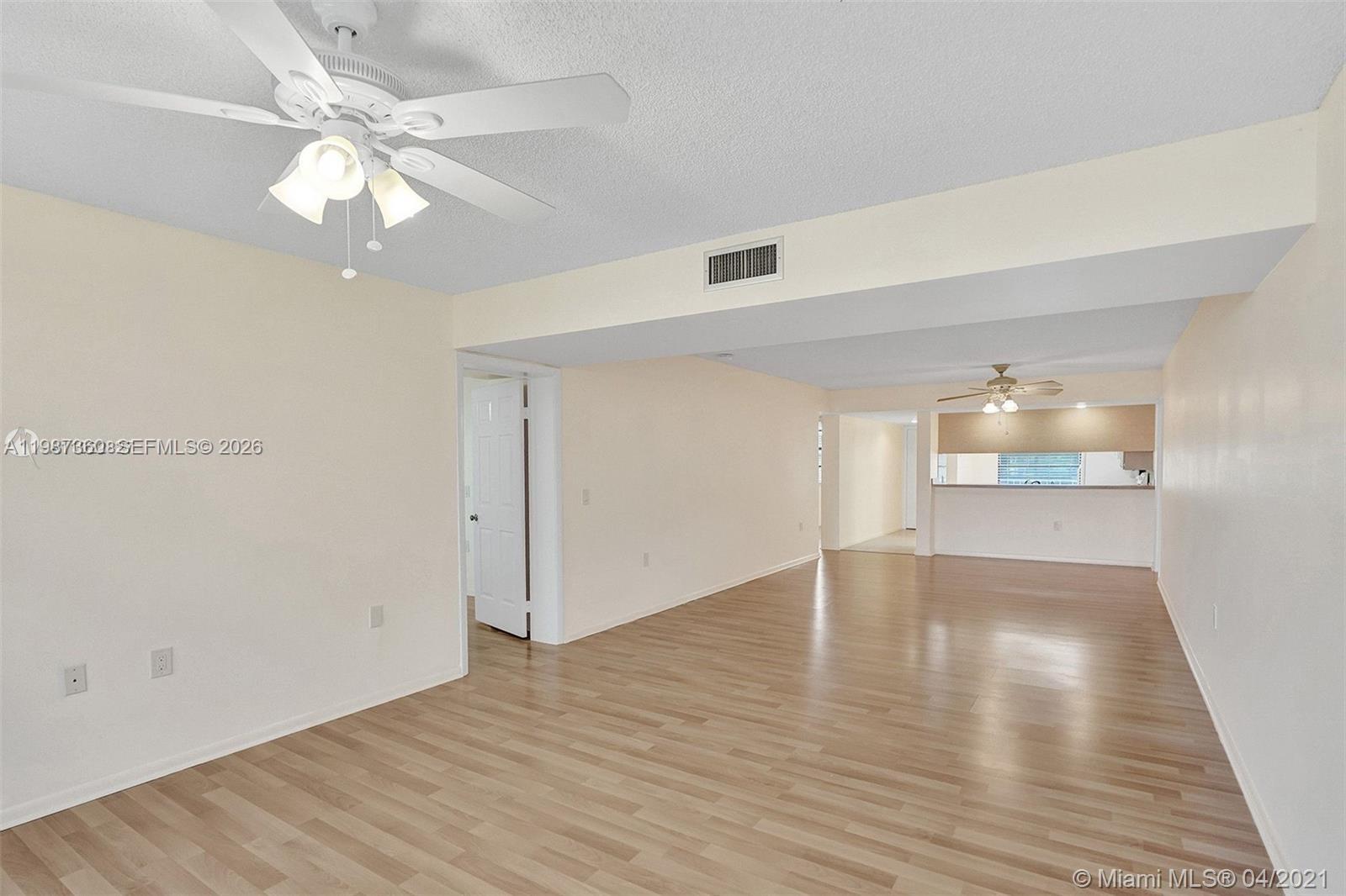 An open-concept living area features light wood-look flooring, white walls, and two ceiling fans — 1715 Whitehall Dr # 202, Davie FL 33324, DAVIE, FL