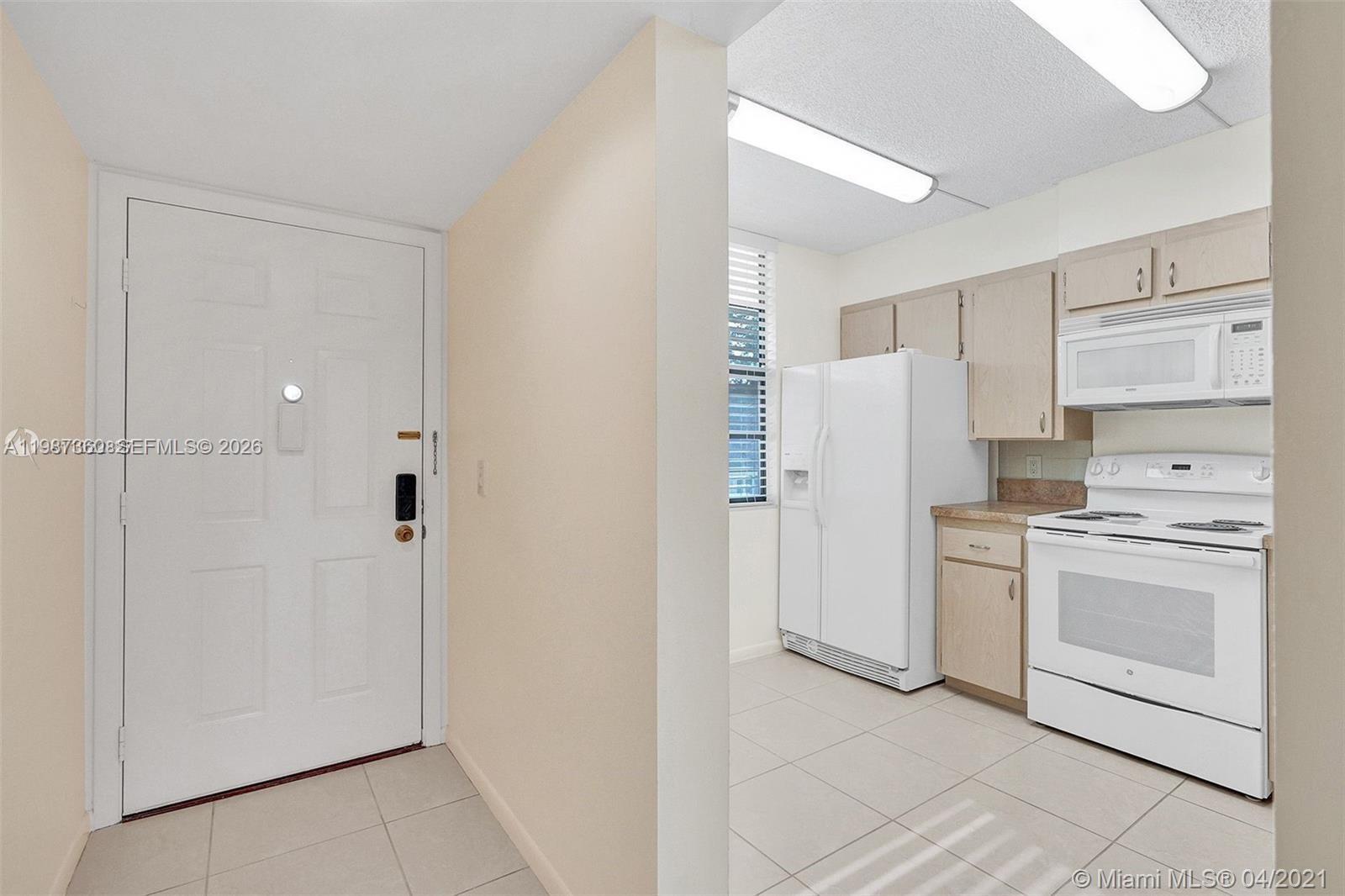 A white front door opens into a kitchen with light-colored cabinets and white appliances — 1715 Whitehall Dr # 202, Davie FL 33324, DAVIE, FL
