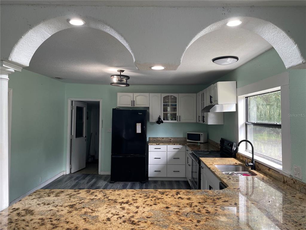A kitchen features light green walls, white cabinets, granite countertops, and a black refrigerator — 3816 LONE OAK ROAD, PLANT CITY, FL