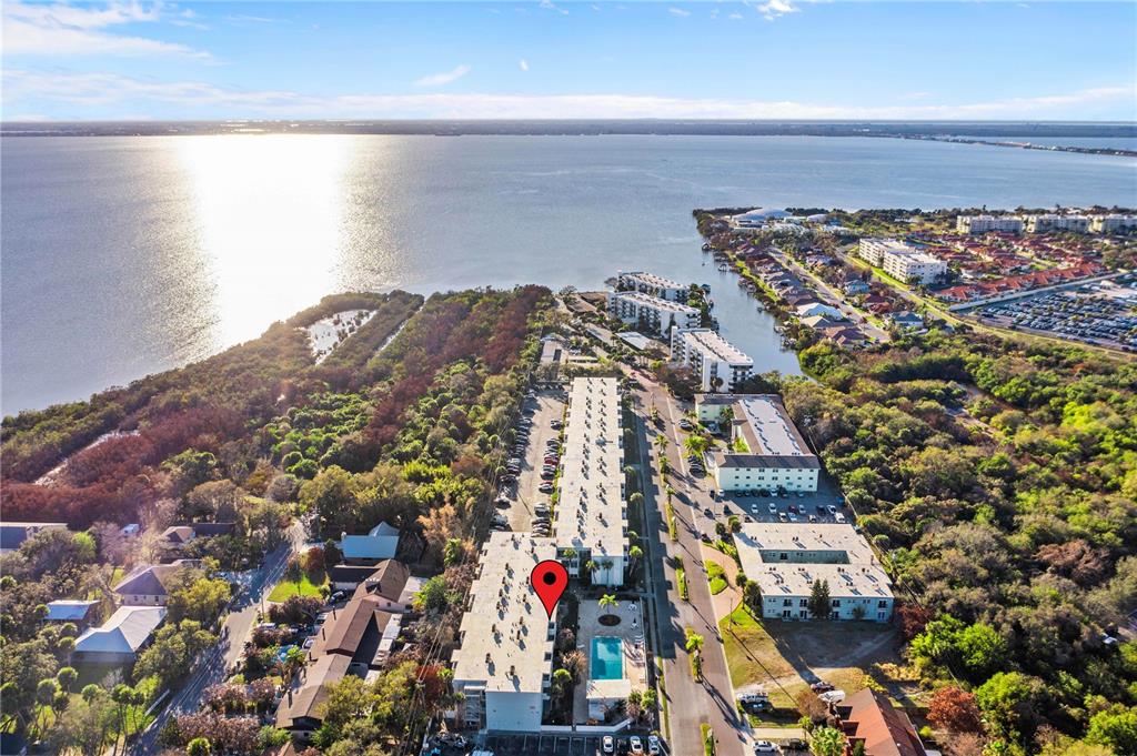 An aerial view shows a multi-story apartment complex with a pool near a large lake — 221 COLUMBIA DRIVE UNIT 340, CAPE CANAVERAL, FL