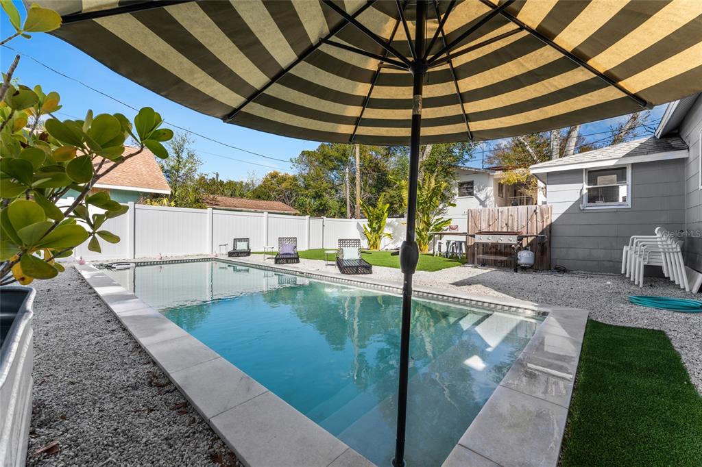 A backyard swimming pool features a striped umbrella, gravel landscaping, and a white privacy fence — 783 30TH AVENUE N, ST PETERSBURG, FL