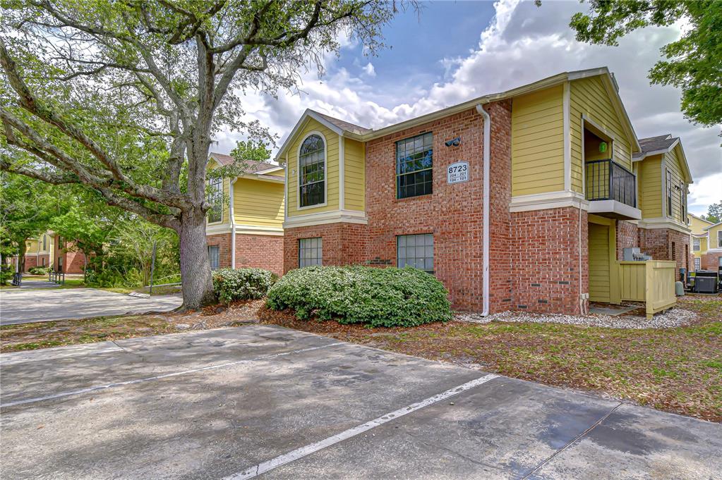 A two-story brick and yellow siding apartment building stands behind a paved parking lot — 8723 FANCY FINCH DRIVE UNIT 201, TAMPA, FL