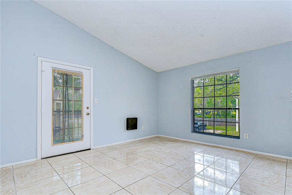 An empty room features light blue walls, large white floor tiles, a glass-paneled door, and a window — 8723 FANCY FINCH DRIVE UNIT 201, TAMPA, FL