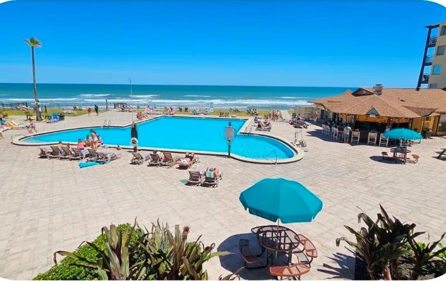 An outdoor swimming pool area overlooks the ocean with a tiki bar and patio seating — 2301 S ATLANTIC AVENUE UNIT 542, DAYTONA BEACH SHORES, FL