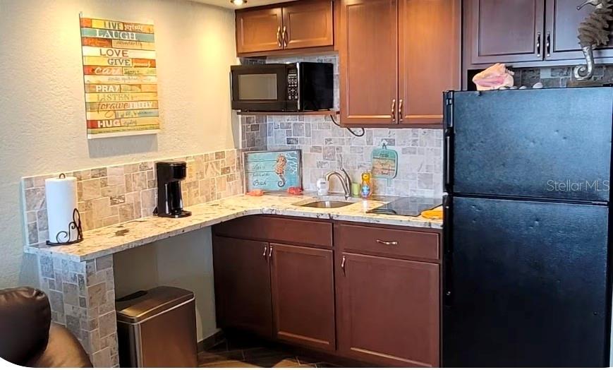 A kitchen features dark wood cabinets, a black refrigerator, and a tiled backsplash — 2301 S ATLANTIC AVENUE UNIT 542, DAYTONA BEACH SHORES, FL