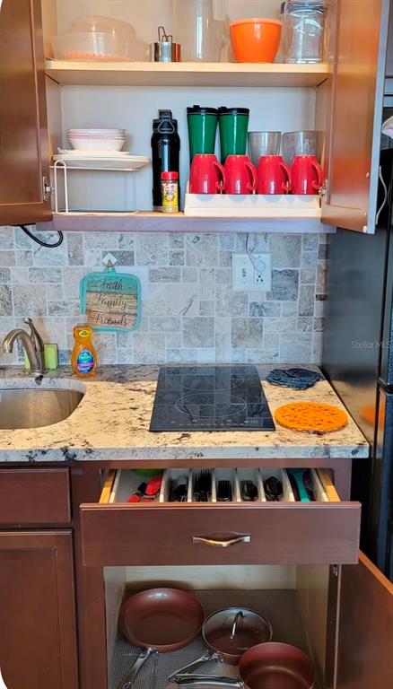 A kitchen features brown cabinets, granite countertops, a cooktop, and an open drawer with utensils — 2301 S ATLANTIC AVENUE UNIT 542, DAYTONA BEACH SHORES, FL