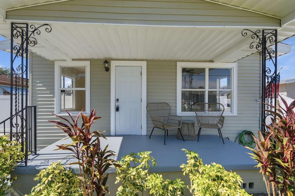 A covered front porch features light green siding, a white door, and two wicker chairs — 2704 W LEROY STREET, TAMPA, FL