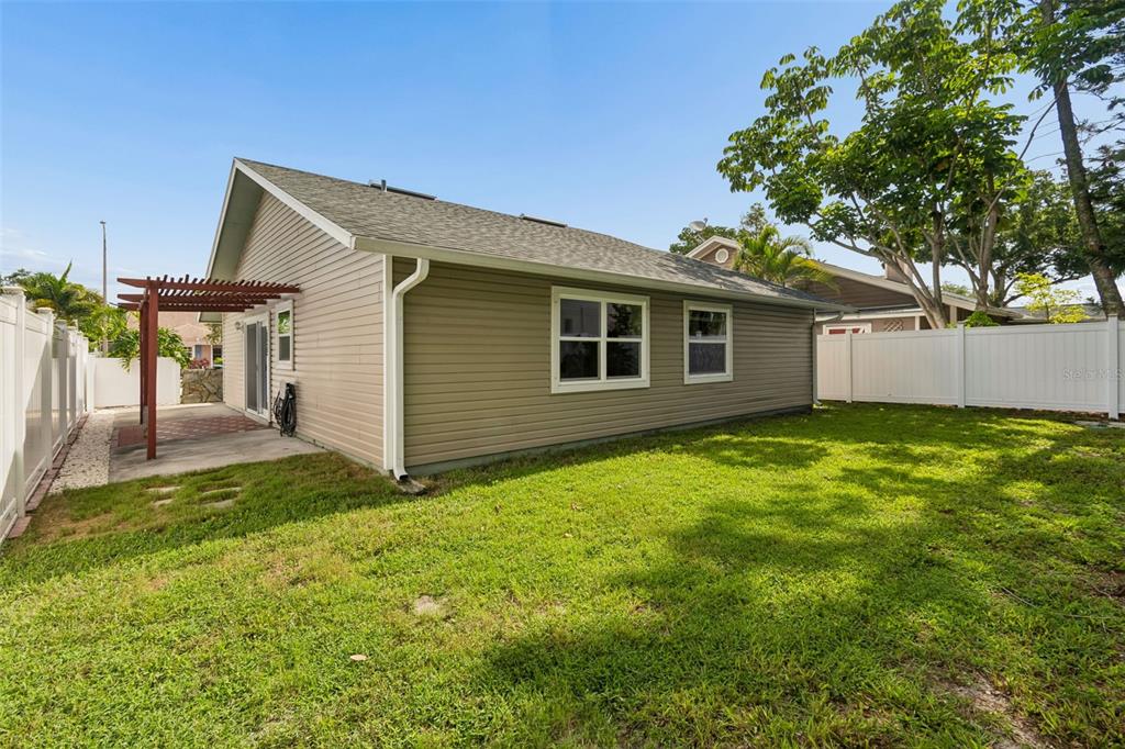 The exterior of a tan-sided house features a small patio with a wooden pergola — 3134 WHISPERING DRIVE N, LARGO, FL