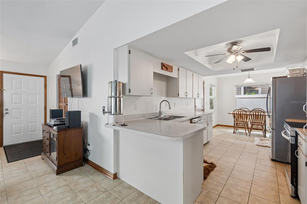 A kitchen with white cabinets, a breakfast bar, and tile flooring opens to a dining area — 3134 WHISPERING DRIVE N, LARGO, FL