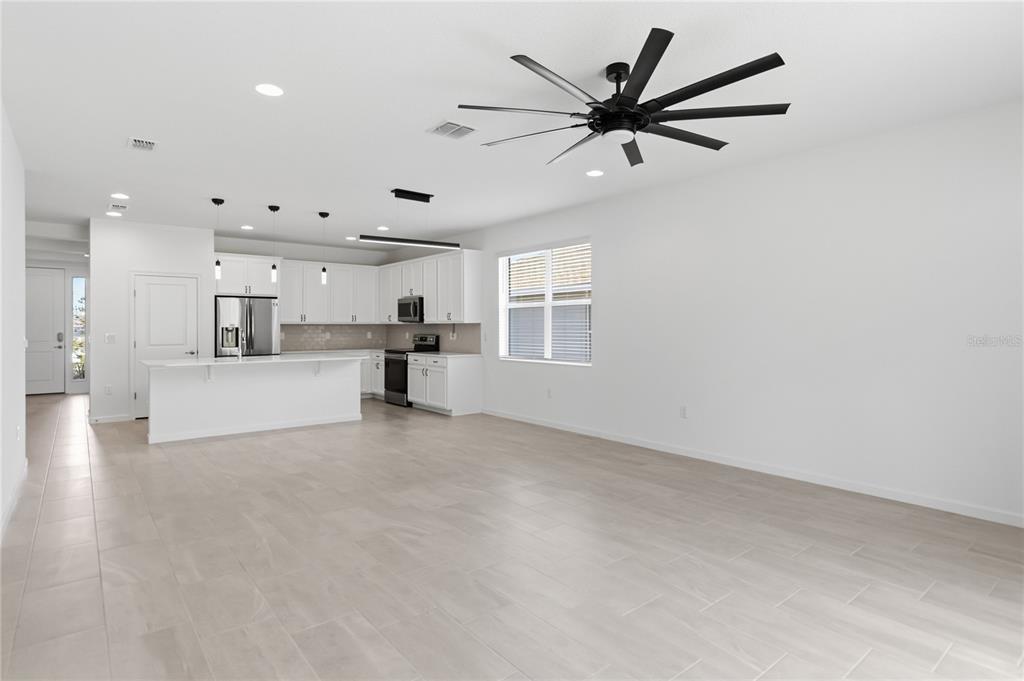 A bright, open-concept kitchen and living area features white cabinetry, stainless appliances, and tile flooring — 413 SAPPHIRE DRIVE, DAVENPORT, FL