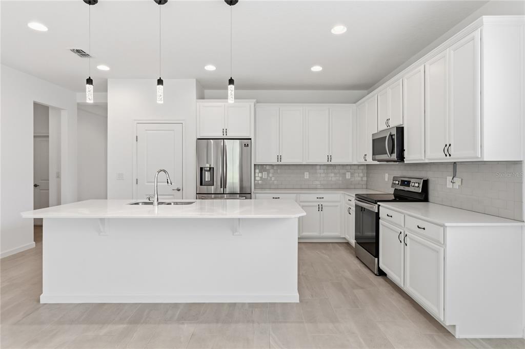 A modern kitchen features white cabinetry, a large center island, and stainless steel appliances — 413 SAPPHIRE DRIVE, DAVENPORT, FL