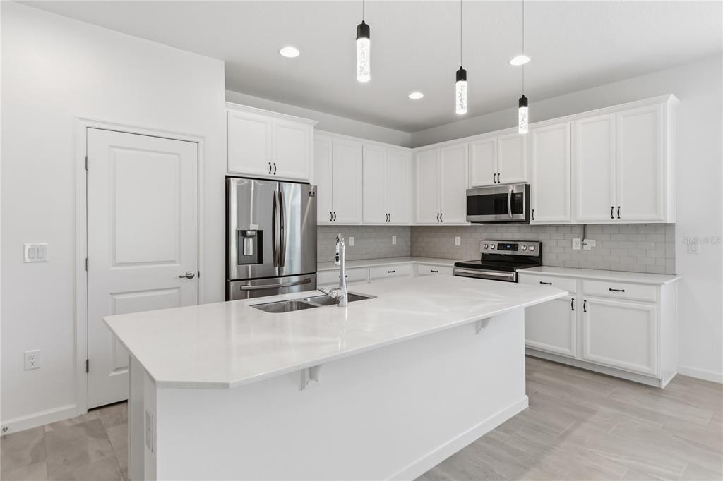 A modern kitchen features white cabinets, a large quartz island, and stainless steel appliances — 413 SAPPHIRE DRIVE, DAVENPORT, FL