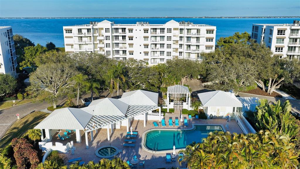 An aerial view shows a swimming pool and clubhouse area in front of waterfront apartment buildings — 2450 HARBOURSIDE DRIVE UNIT 234, LONGBOAT KEY, FL
