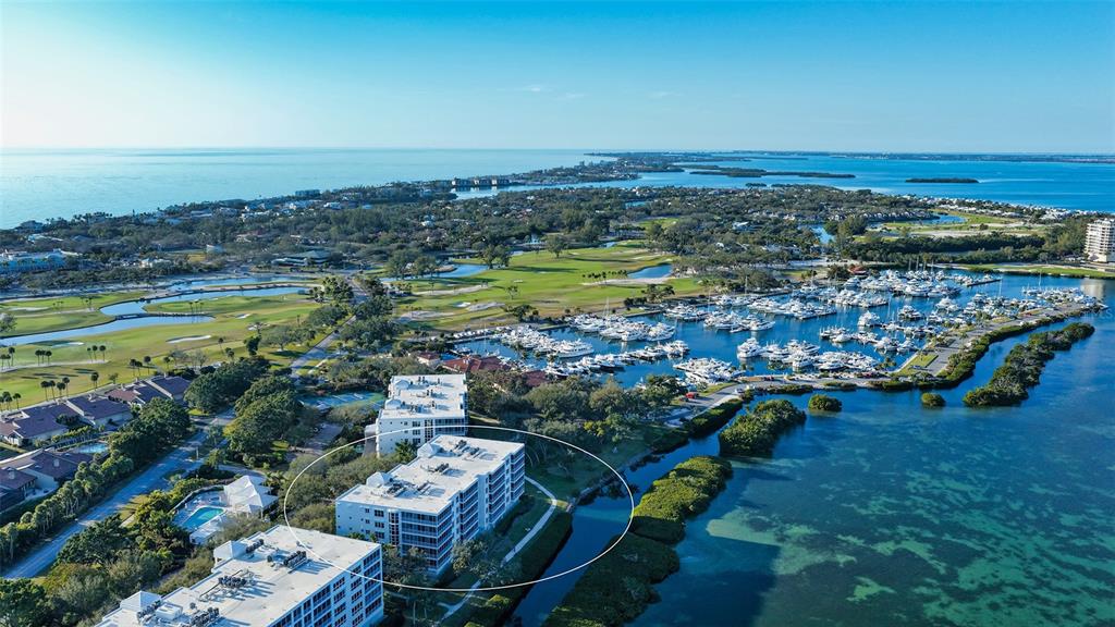 An aerial view shows a multi-story apartment building surrounded by a golf course and marina — 2450 HARBOURSIDE DRIVE UNIT 234, LONGBOAT KEY, FL