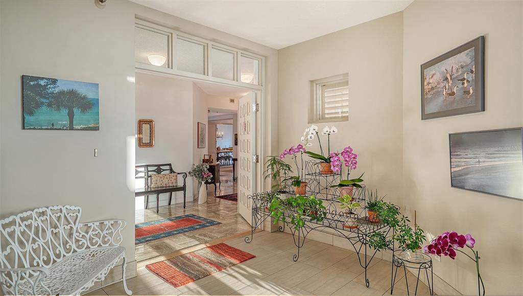 A bright entryway features a white metal bench, a tiered plant stand, and tiled floors — 2450 HARBOURSIDE DRIVE UNIT 234, LONGBOAT KEY, FL