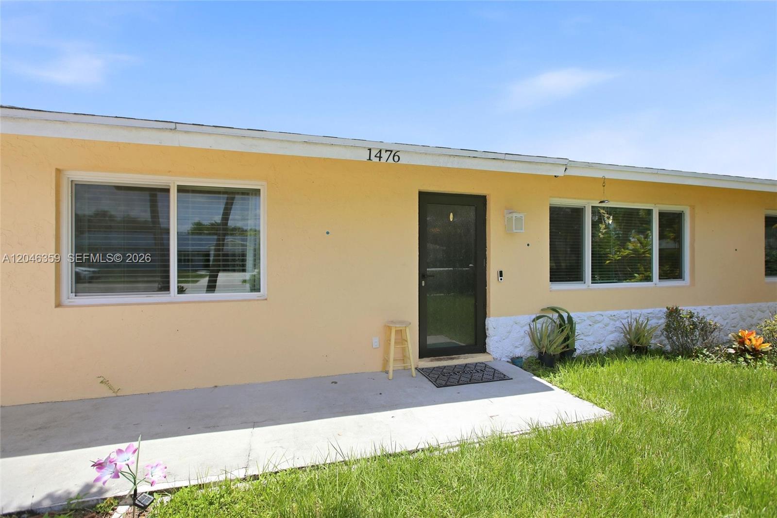 The exterior of a single-story house features yellow stucco walls, a concrete porch, and windows — 1476 N Mangonia Dr, West Palm Beach FL 33401, WEST PALM BEACH, FL