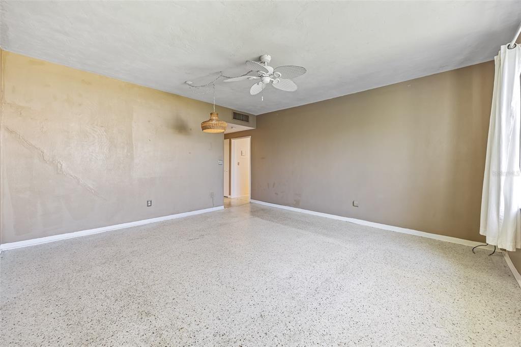 An empty room features tan walls, a white ceiling fan, a wicker pendant light, and terrazzo flooring — 55 SEA PARK BOULEVARD UNIT 309, SATELLITE BEACH, FL