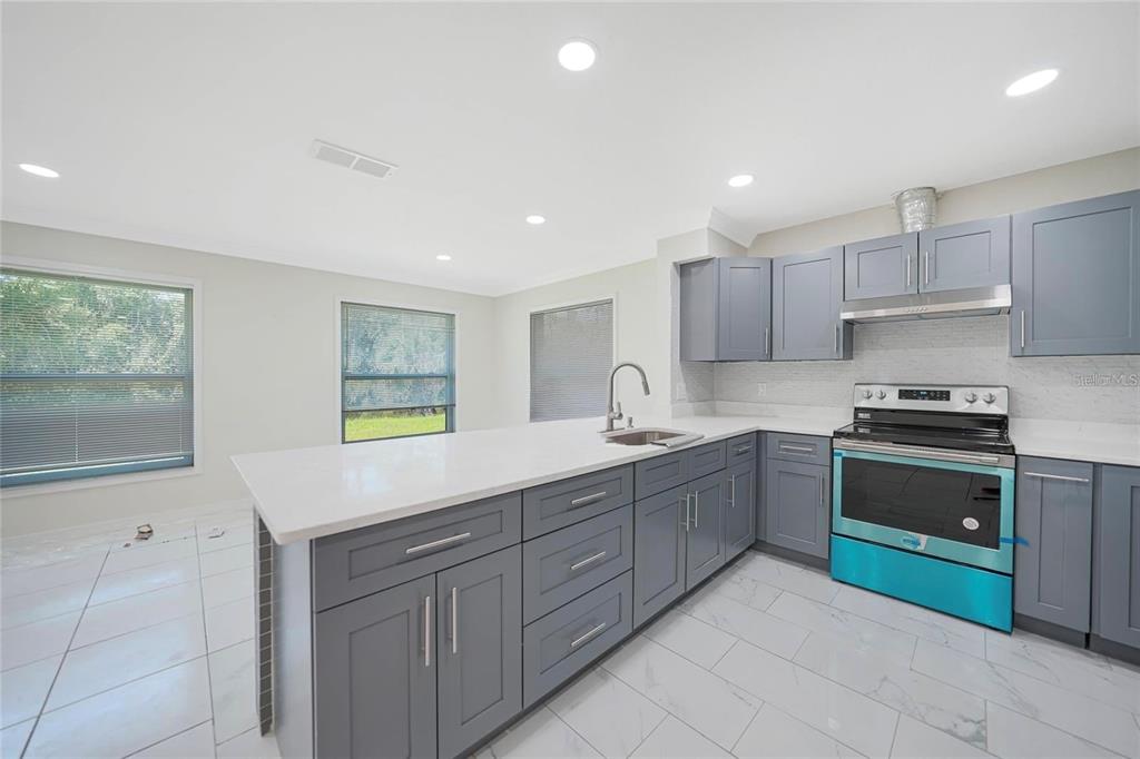 A modern kitchen features gray cabinets, white countertops, stainless steel appliances, and white tile flooring — 351 & 359 KINDRED BOULEVARD, PORT CHARLOTTE, FL