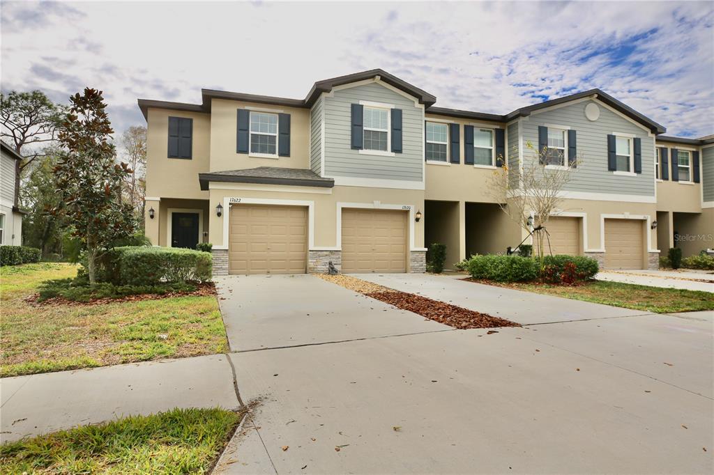 A two-story townhouse exterior features tan stucco, blue siding, and two attached garages — 17620 NECTAR FLUME DRIVE, LAND O LAKES, FL
