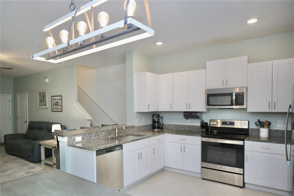 A kitchen with white cabinets, granite countertops, stainless steel appliances, and a hanging light fixture — 17620 NECTAR FLUME DRIVE, LAND O LAKES, FL