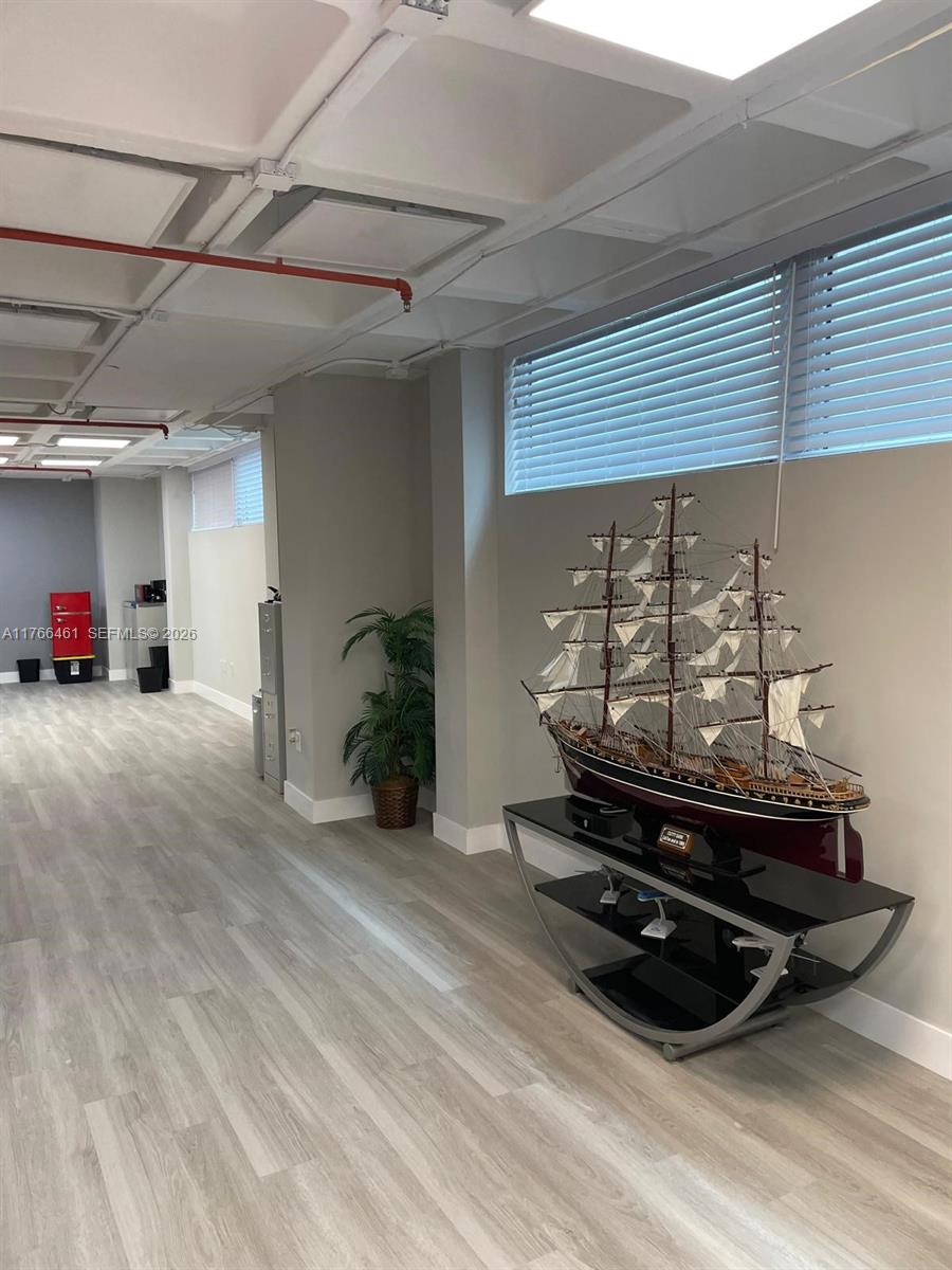 A modern office space features light wood-look flooring, exposed ceiling pipes, and a large model ship — 4300 Biscayne Blvd # G06, Miami FL 33137, MIAMI, FL