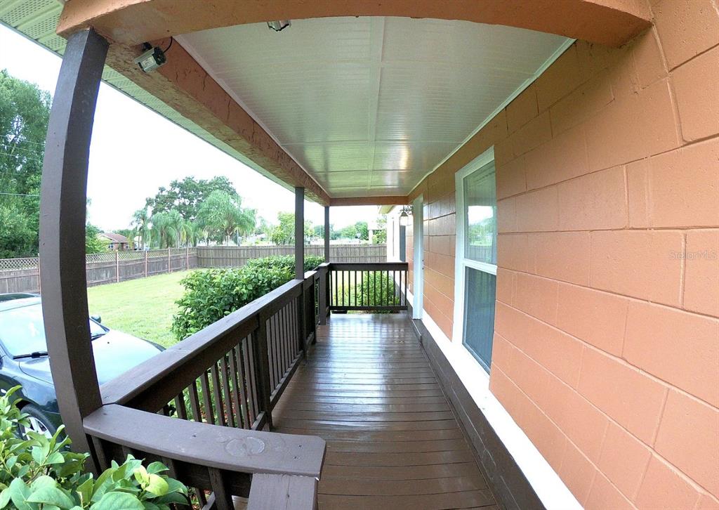 A covered wooden porch with railings overlooks a grassy yard next to a block wall — 1316 GRAYSON DRIVE, ORLANDO, FL