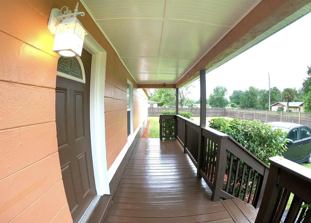 A covered wooden porch with dark railings runs along the side of a peach-colored house — 1316 GRAYSON DRIVE, ORLANDO, FL
