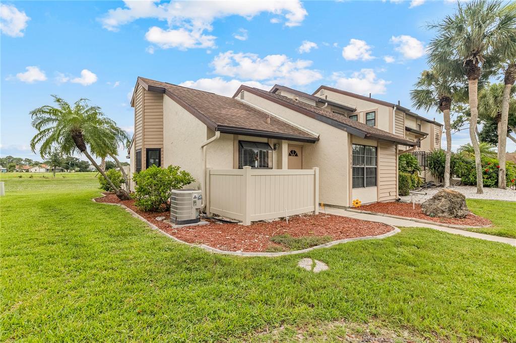 A tan, multi-level townhouse exterior features a small fenced patio, an air conditioning unit, and landscaping — 5500 NIBLICK PLACE, NORTH PORT, FL