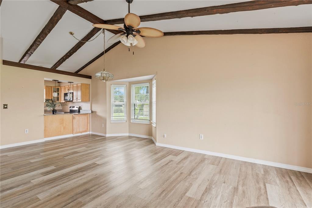 A living room with vaulted ceilings, exposed wooden beams, and light-colored wood-look flooring — 5500 NIBLICK PLACE, NORTH PORT, FL