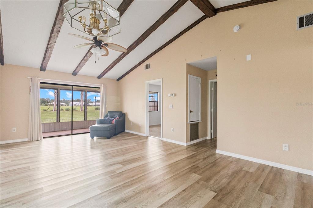 A living room with vaulted ceilings, exposed wooden beams, light wood flooring, and a sliding door — 5500 NIBLICK PLACE, NORTH PORT, FL