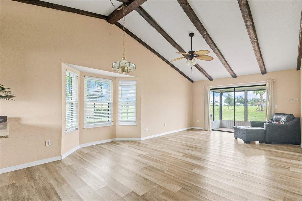 A living room with vaulted ceilings, exposed wooden beams, light wood flooring, and sliding doors — 5500 NIBLICK PLACE, NORTH PORT, FL