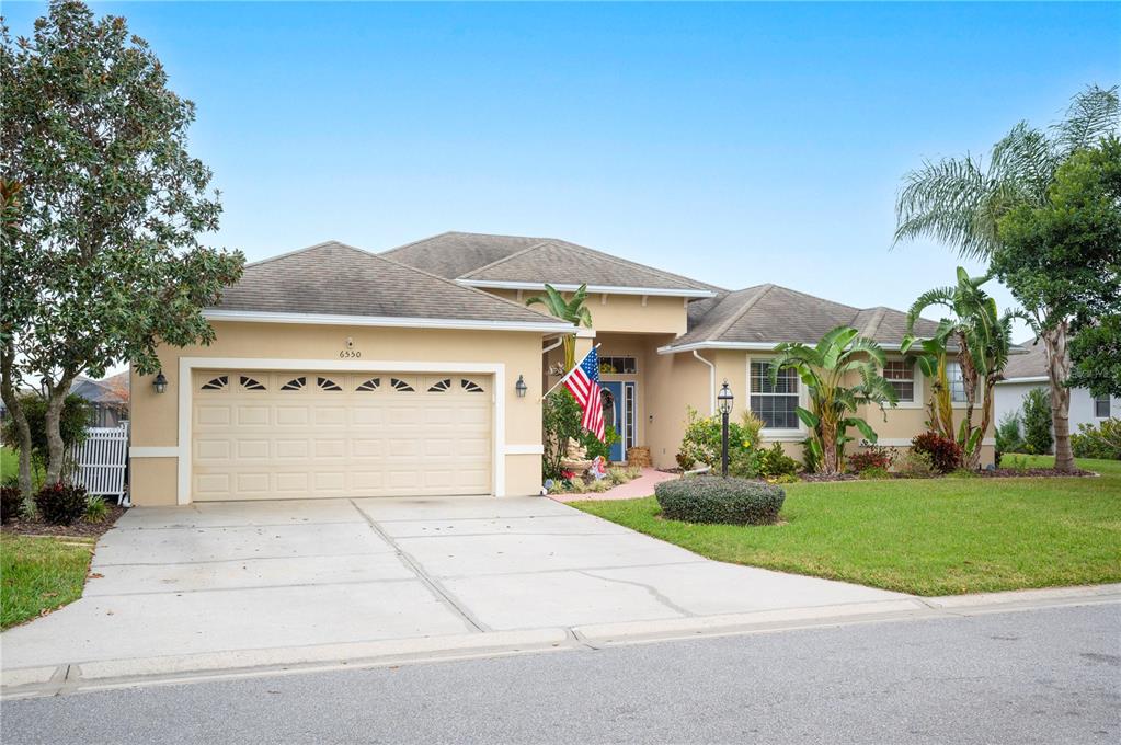 A single-story suburban house with a tan stucco exterior, a two-car garage, and landscaping — 6550 EVERGREEN PARK DRIVE, LAKELAND, FL