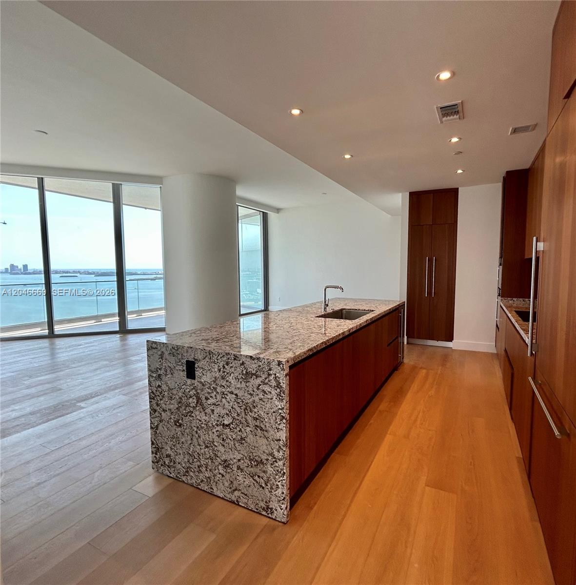 A modern kitchen features a granite island, wood cabinetry, and floor-to-ceiling windows with water views — 175 SE 25th Road # 2804, Miami FL 33129, MIAMI, FL