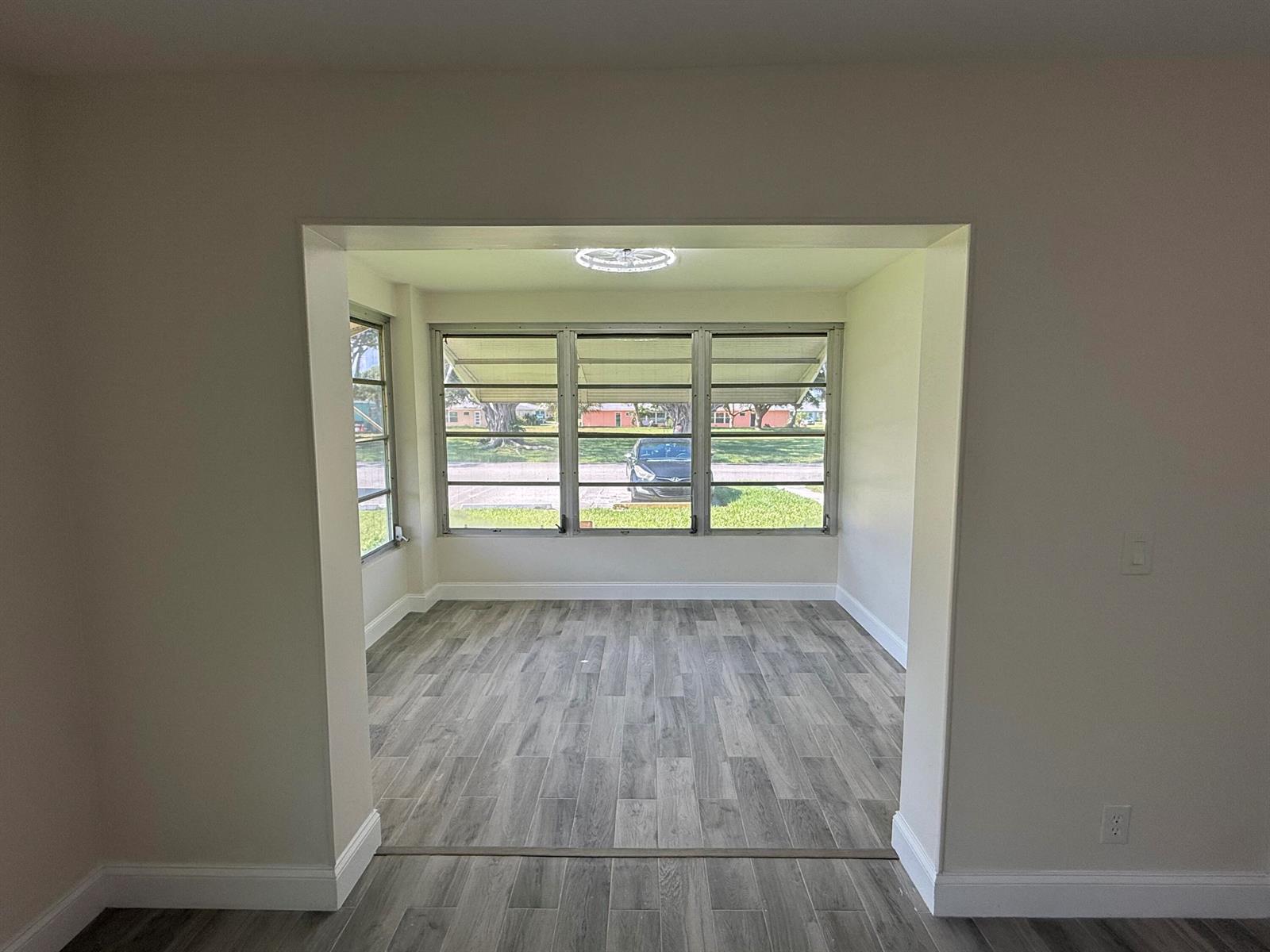 A sunroom with gray wood-look flooring and large windows overlooks a street and parked car — 255 South Boulevard # D, Boynton Beach FL 33435, BOYNTON BEACH, FL