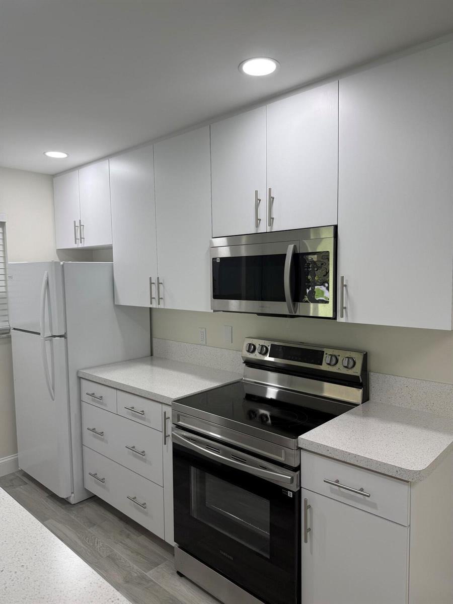 A kitchen features white cabinets, stainless steel appliances, and light-colored speckled countertops — 255 South Boulevard # D, Boynton Beach FL 33435, BOYNTON BEACH, FL
