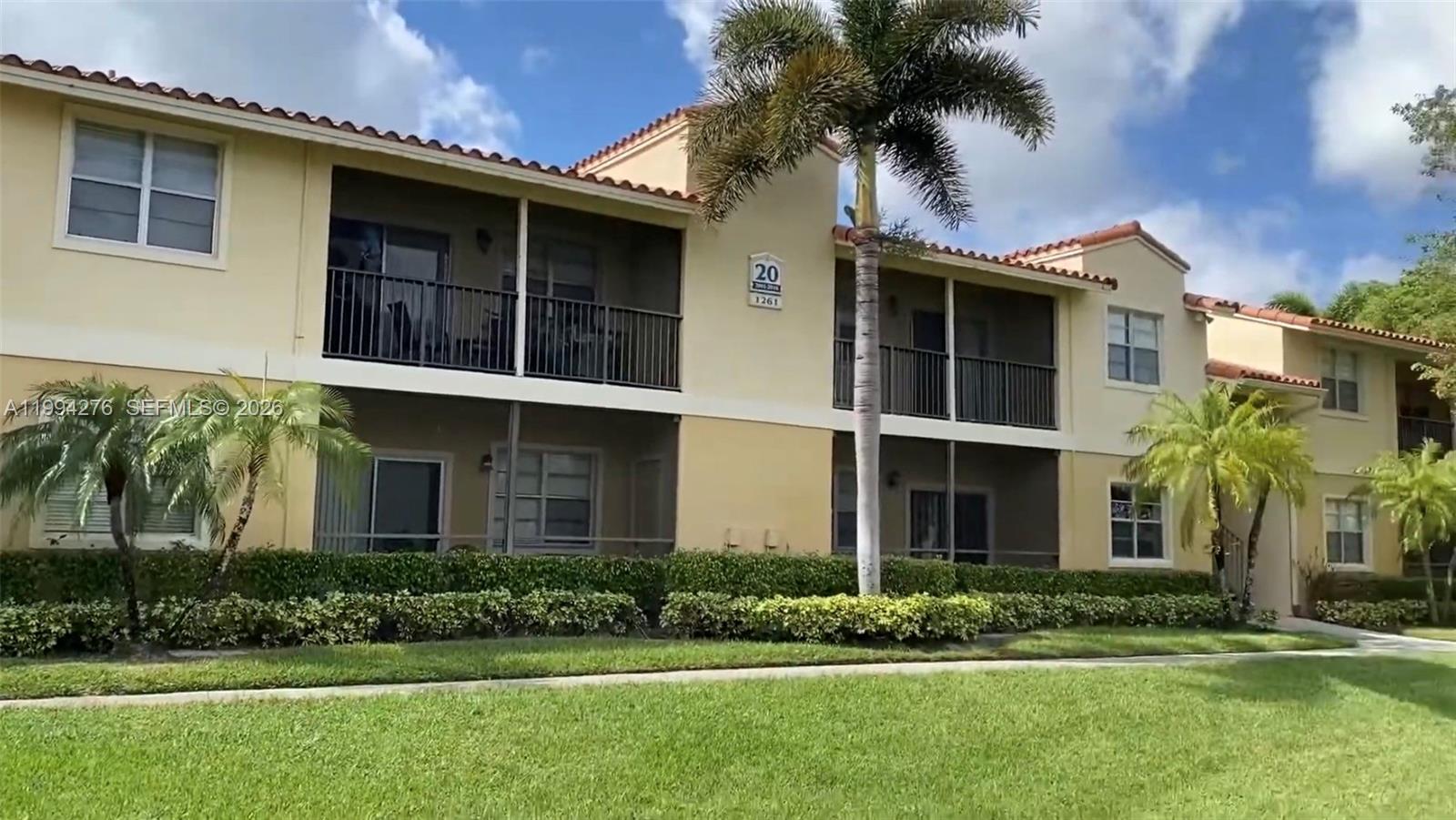 A two-story apartment building features beige stucco walls, screened balconies, and a tile roof — 1261 SW 46th Ave # 2016, Pompano Beach FL 33069, POMPANO BEACH, FL