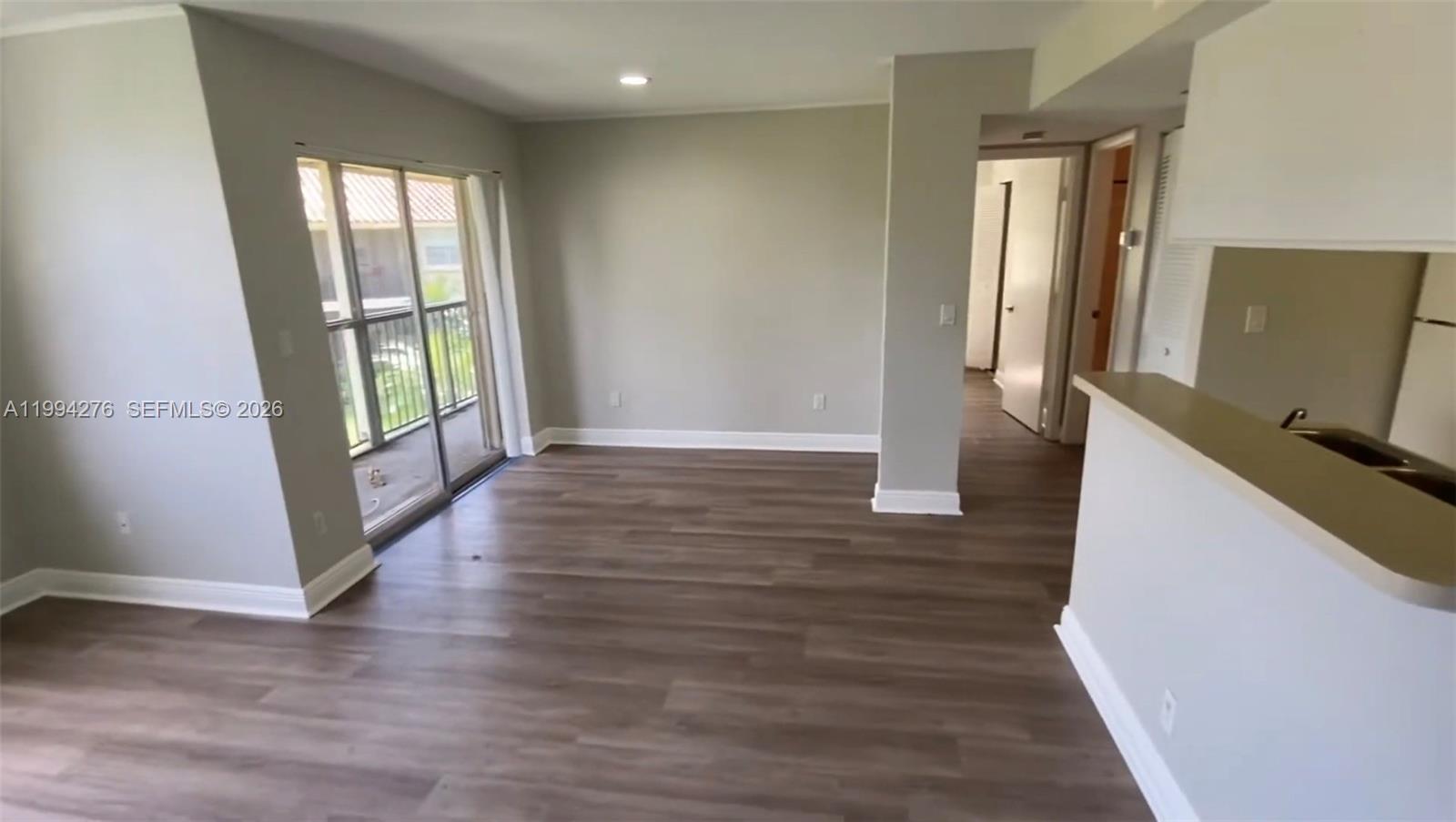 This living area features wood-look flooring, light gray walls, and a sliding glass balcony door — 1261 SW 46th Ave # 2016, Pompano Beach FL 33069, POMPANO BEACH, FL