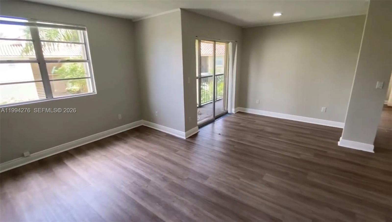 An empty room features light gray walls, wood-look flooring, a window, and sliding glass doors — 1261 SW 46th Ave # 2016, Pompano Beach FL 33069, POMPANO BEACH, FL