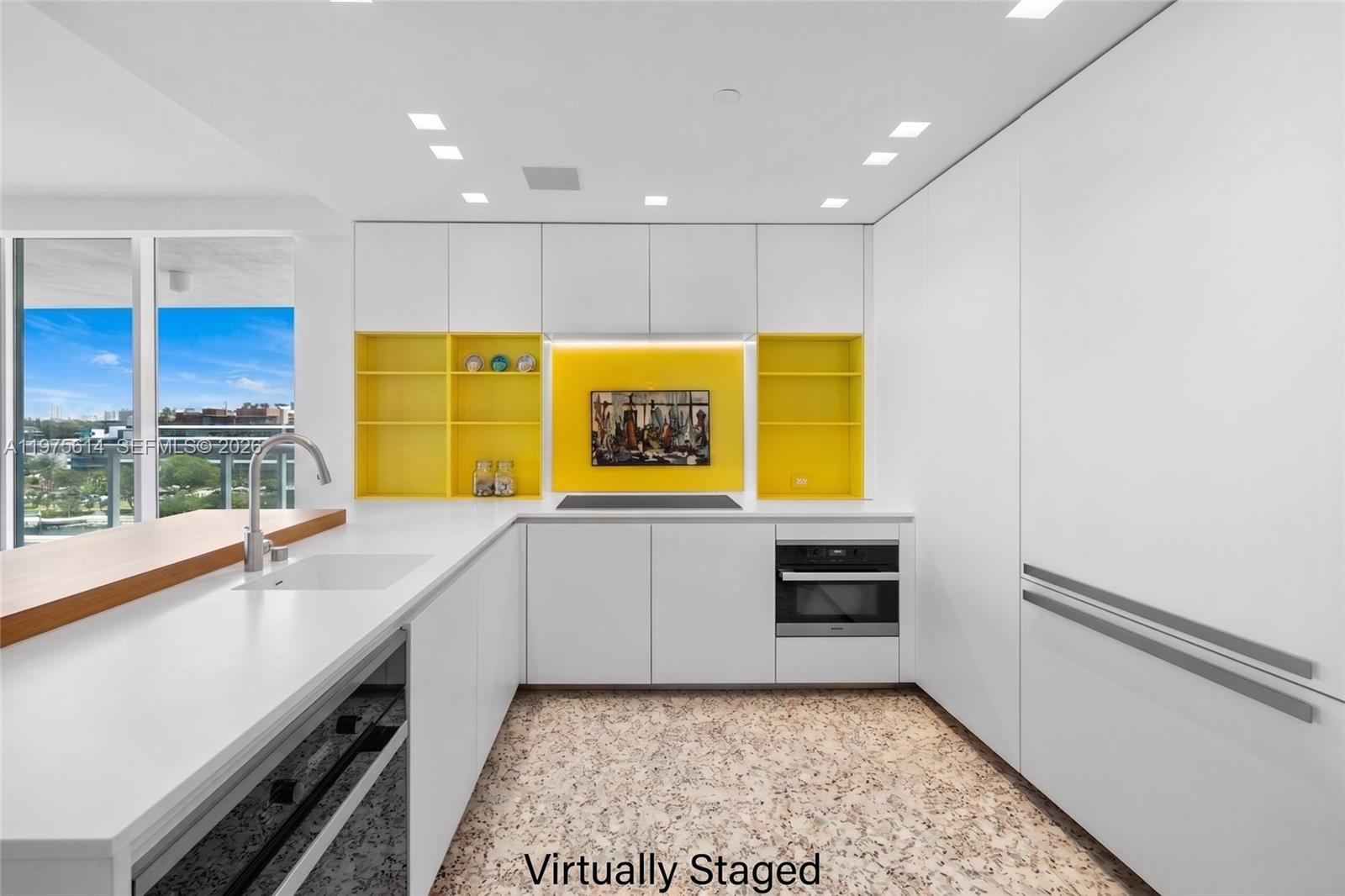 A modern kitchen features white cabinetry, yellow open shelving, a terrazzo floor, and a balcony view — 10 Venetian Way # 904, Miami Beach FL 33139, MIAMI BEACH, FL